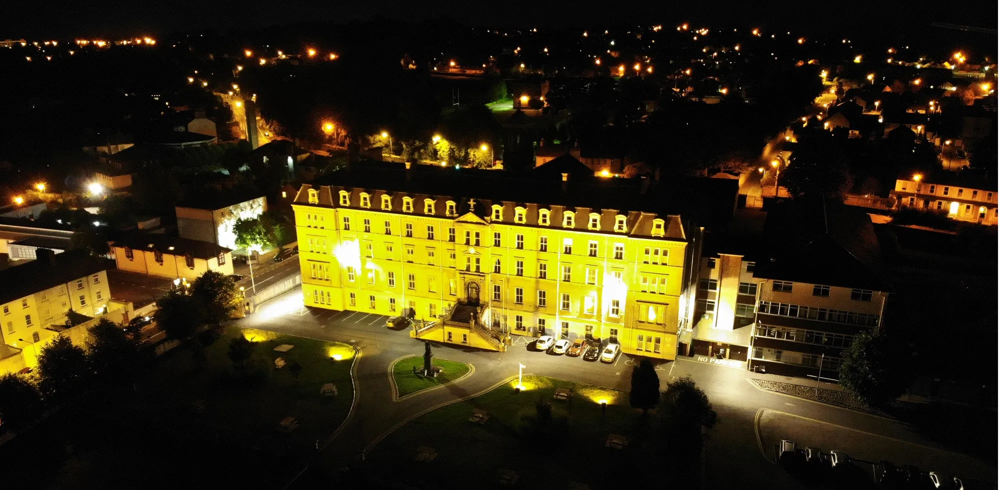 The college floodlit at night, photographed from the air above Newtown with the lights of Waterford behind it